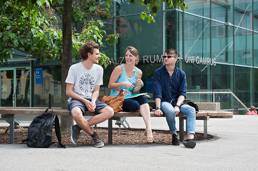 Students sitting in front of the lecture halls at the Campus.