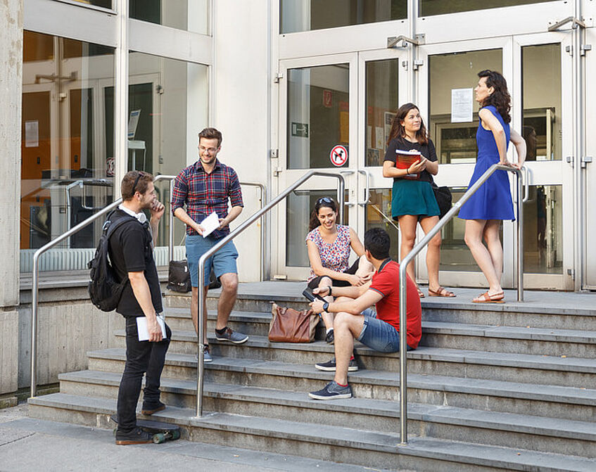 Students are standing or sitting on the steps in front of the OMP building.