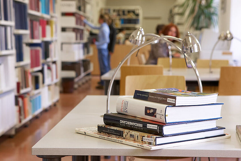 Foto zeigt gestapelte Bücher in einer Bibliothek.