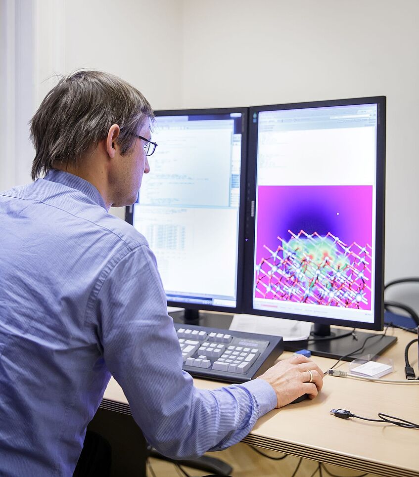 Professor is sitting in front of two computer screens.