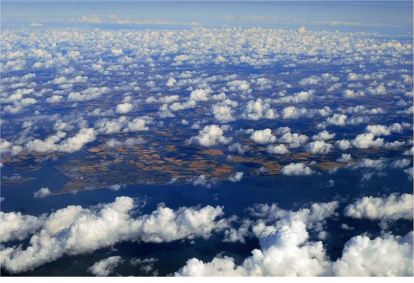 Sicht von oben auf Wolken über dem Boden und dem Meer.