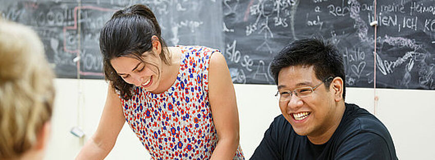 Das Bild zeigt zwei lächelnde Studierende vor einer Tafel