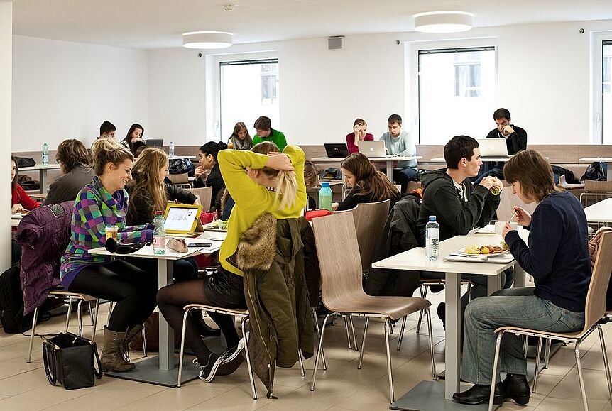 StudentInnen sitzen in einem Aufenthaltsbereich, wo man Lernen, Essen, etc. kann.