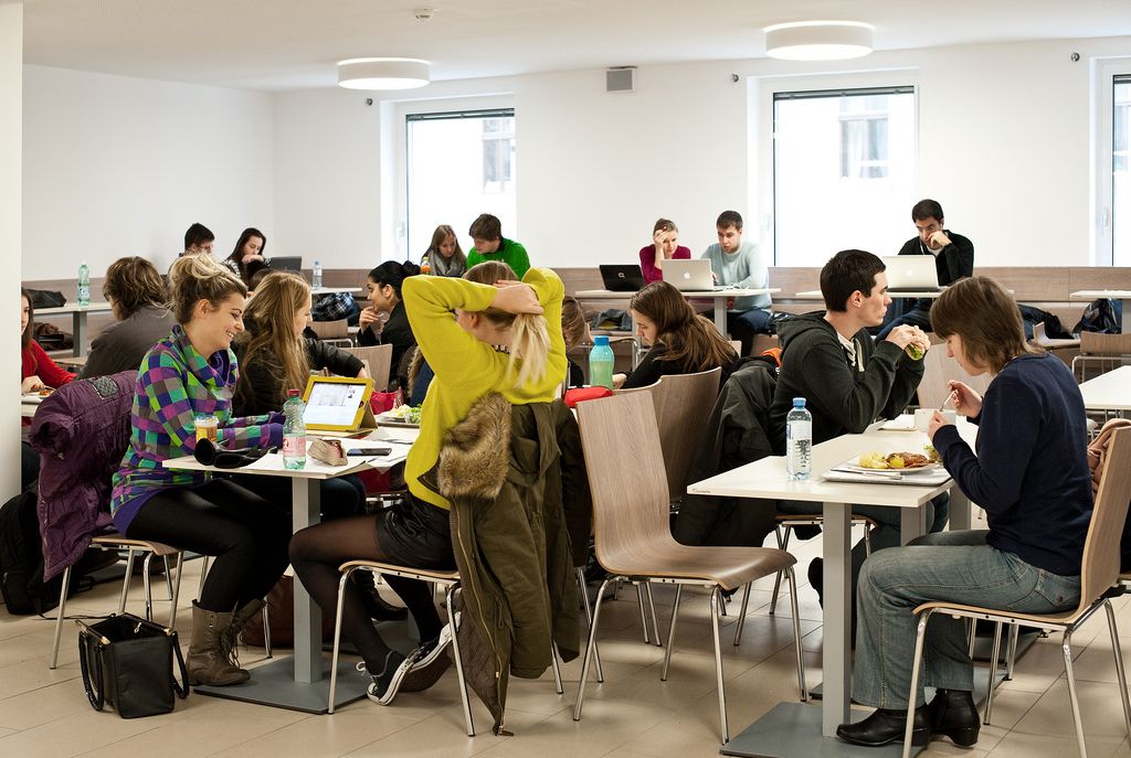 StudentInnen sitzen in einem Aufenthaltsbereich, wo man Lernen, Essen, etc. kann.